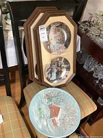 Two framed sets of collector plates on a chair with the ceramic wall decor piece nearby.