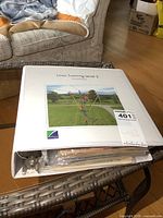 White binder filled with vintage comic books placed on a wicker table, showing signs of wear and stacked comics inside plastic sleeves.