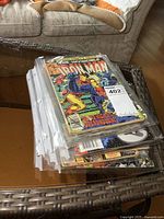 Stack of vintage Marvel comic books in clear plastic sleeves on a wicker table, showing mostly Iron Man on top