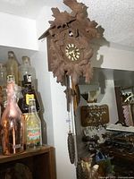 Clock mounted on wall showing wooden carvings of leaves and birds, pinecone weights, and pendulum.