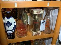 Photo of four vintage bottles on shelf including Calnans Dairy, Peoples Dairy, Coca-Cola commemorative, and Leafs bottle with shirt cover