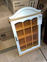 Front view of small wooden display case with glass door and decorative top molding, showing interior divided into small shelves.