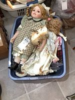 Basket filled with assorted porcelain dolls, some with fabric clothing, including a tall doll with braided hair and several others partially visible.