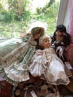 Four porcelain dolls on a ledge against window with garden background, showing full clothing and hair styles