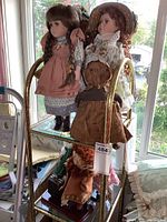 Porcelain and vintage dolls displayed on glass shelves in front of window, showing details of clothing and hair