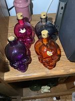 Four different colored glass skull bottles arranged on wood surface, visible details on colors and cork stoppers