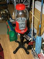 Full view of metal and glass gumball machine on black stand with surrounding items