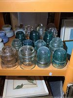 Shelf view showing multiple glass insulators in clear and greenish-blue colors, some ribbed, some smooth.