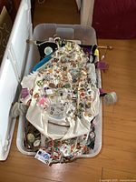 Large collection of pins attached to various fabrics including a white shirt, in a plastic bin.