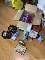 Full view of the open box containing various metal lunch boxes, tins, toys, and stuffed animals on the floor around it