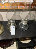 Front view of two glass oil lamps with chimneys showing entire lamps and metal burners