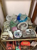 Overview of all glass figures and paperweights showing various bird shapes, a dolphin, and paperweights on a glass shelf