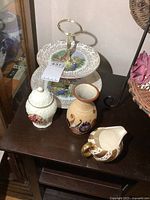 Photo showing pottery vase, two-tier serving plate, porcelain jar, and creamer on a dark wooden surface.