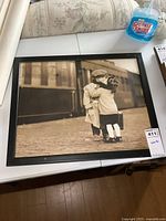 Framed sepia-tone photo print showing two children hugging at a train station, viewed from a distance.