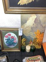 Two tall signed prints including a mountain landscape and floral print, with three candles in front