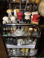 Three-tier metal cart filled with various salt and pepper shakers; novelty mushroom, character, black face designs, glass, and ceramic types.