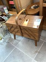 Side angled view of the closed vintage wooden sewing stand showing the tiered accordion-style compartments and central handle