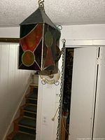Photo of the stained glass hanging light suspended showing geometric colored glass panels and metal frame with chain attached.