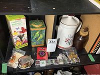 Overview of lot items on black shelving showing teapot, jewelry, tin, rocks, solar butterfly, and brown jar with cork.