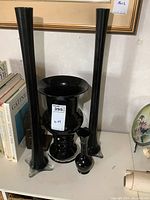 Four black glass vases displayed including two tall black straight vases, one large flared black amethyst vase, and one smaller ruffled rim vase.