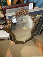 Frontal view of the ornate framed mirror leaning against stacked framed art.