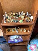 Top shelf wooden cabinet with an array of small ceramic animal and nursery rhyme Wade figures, placed in rows.
