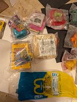 Ten McDonald's Happy Meal toys in sealed packaging laid out together, showing variety of characters and packaging styles.