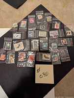 Photo of all 25 postage stamps arranged on black cloth, each in individual sealed plastic bags, showing variety of designs and colors.