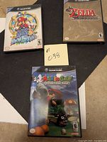 Three GameCube game cases laid flat: Super Mario Sunshine, Zelda Wind Waker, Mario Golf Toadstool Tour.