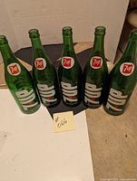 Front view of five green 7UP glass bottles standing in a row on a white surface.