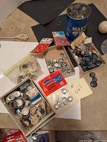 Overview of three containers filled with assorted buttons including a metal can and two boxes with different sizes and types of buttons.