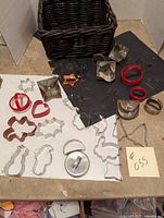 Overall view of 32 metal cookie cutters spread around two surfaces with a dark woven basket visible behind.