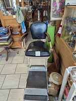 Front view of antique dentist chair showing black cushioned seating and footrest.