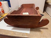 Side view of wooden doll cradle showing rocker bottom and one leg, wood grain visible, minor wear on edges.