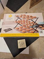 Box front showing assembled multi-tier folding cooling grid with baked goods on tiers and measurements 40.6 x 25.4 cm (16 x 10 in) and assembled height 29.2 cm (11.5 in)