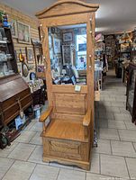 Full view of tall oak hall stand with mirror and storage seat in an antique store.
