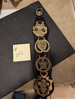 Photo of entire leather belt with four brass horse brasses displayed vertically