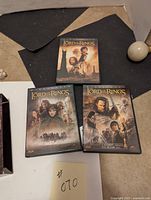 Three DVD cases of The Lord of the Rings trilogy arranged on a dark surface showing the cover art with main characters and titles visible.