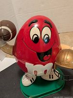 Front view of red M&M dispenser holding football and helmet showing facial expression and base