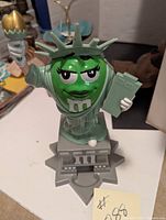 Front view of the green M&M Statue of Liberty dispenser showing the torch, book, and face.