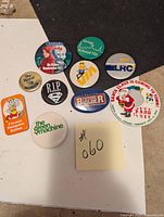 Top view of the 10 assorted metal buttons on a black surface showing various graphics and logos.