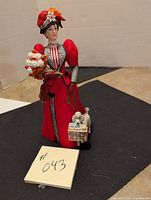 Porcelain figurine of a woman in a detailed red and white Victorian-style dress holding flowers and a gift box with a poodle figurine.