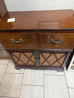 Front view of the wooden cabinet showing two drawers with ornate handles and lower speaker section covered by crisscrossed mesh.
