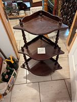 Full view of the assembled 3-tier wooden corner shelf sitting on the floor with visible wear on surfaces.