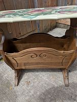 Front angled view showing wooden magazine rack with carved decorative front and hand-painted floral top.