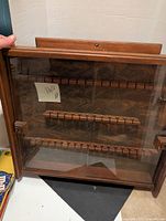 Front view of wooden spoon rack with glass door showing wooden bars inside and decorative backing.