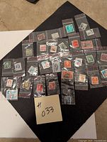 Collection of approximately 30 different postage stamps displayed on a dark cloth, each individually bagged in small clear plastic bags.