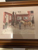 Photo of framed print showing a winter scene with a girl and a palomino horse next to a red building.