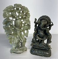 Photo showing two carved stone statues: dark stone Indian god Ganesha and light green Chinese floral design statue.
