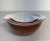 Three nested brown Pyrex mixing bowls with autumn harvest fruit pattern and white interior